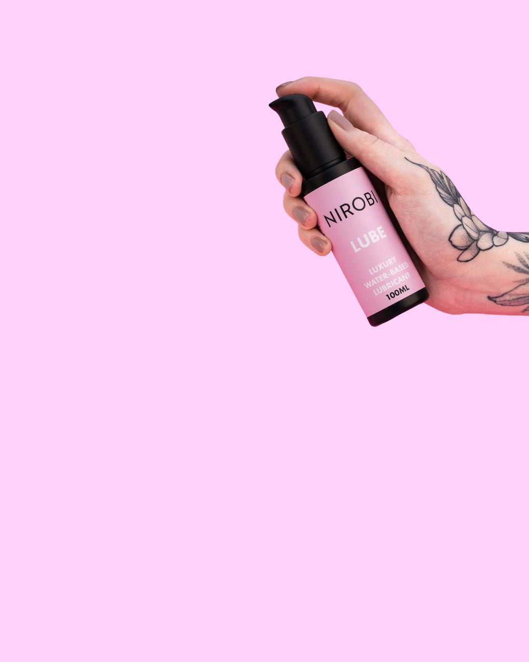 Tattooed hand holding a pink Nirobi water-based lubricant pump bottle against a pale pink background.